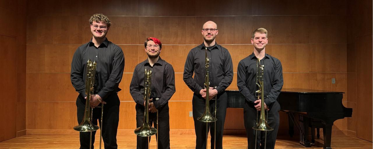 Four trombone students posing with trombones on stage.